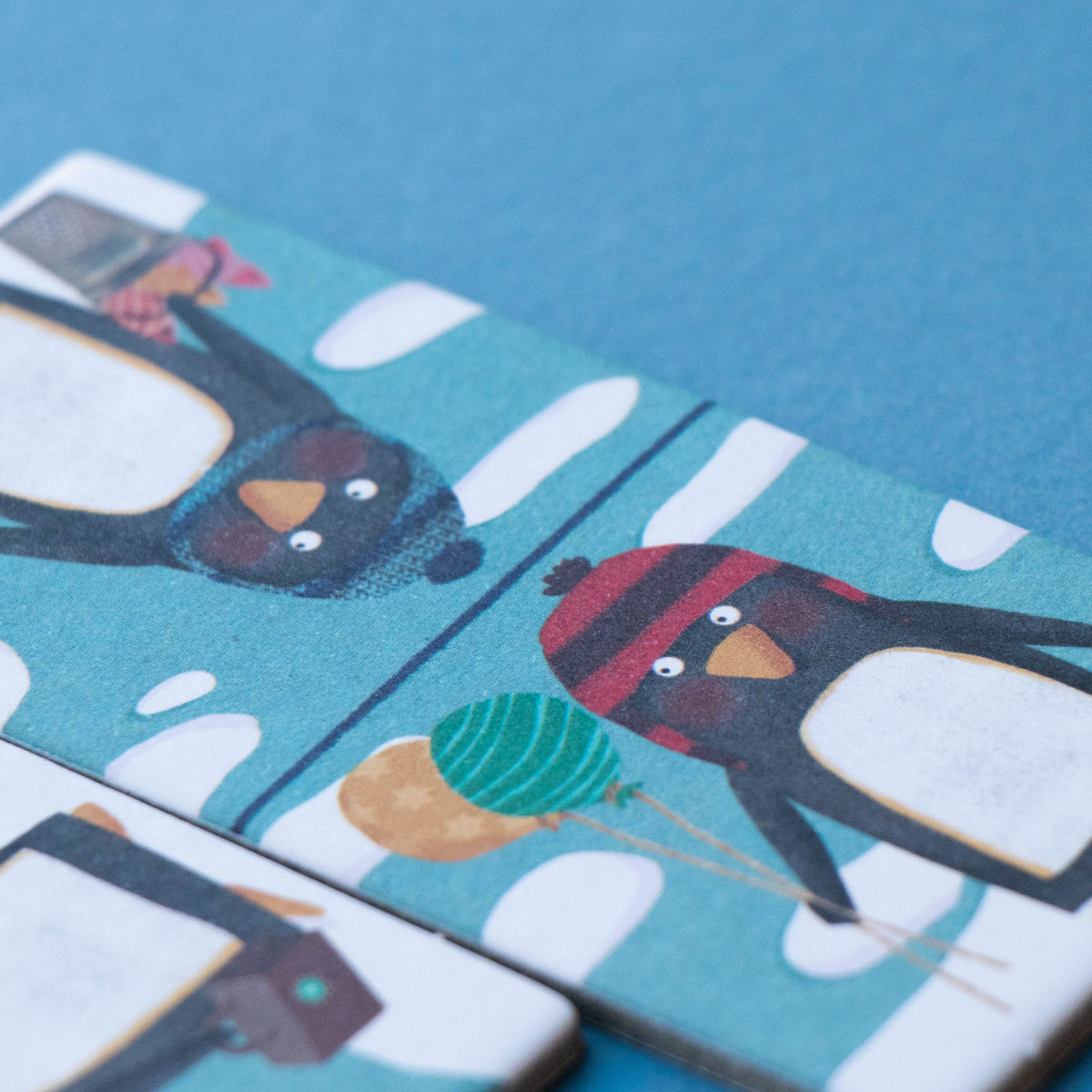 Close-up of Londji domino pieces featuring penguins in winter gear – Two domino tiles featuring adorable penguins in warm scarves and hats.