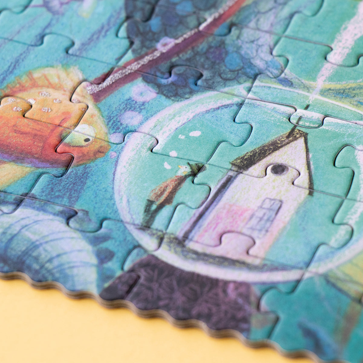 Close-up of a completed Londji My Mermaid puzzle, featuring a whimsical underwater scene with a tiny house inside a bubble, a curious fish, and glitter details.