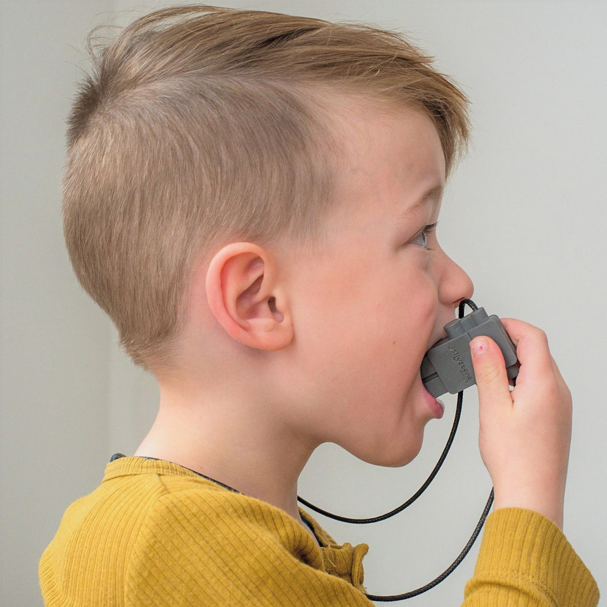 Child wearing a mustard yellow top, chewing on a Jellystone Designs robot pendant.