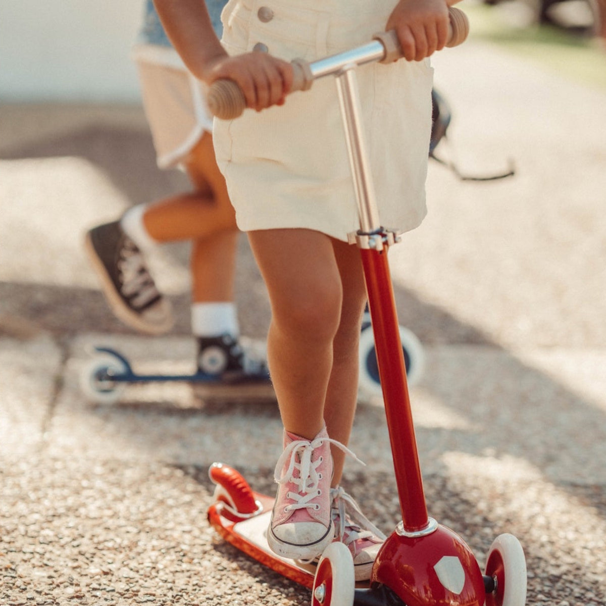 Close-up of a child wearing pink sneakers riding a red three-wheeled scooter outdoors.