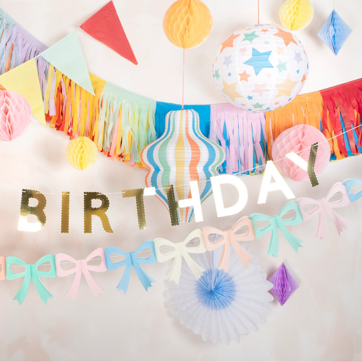 Festive party setup featuring a fringe garland, paper lanterns, and a silver Birthday banner.