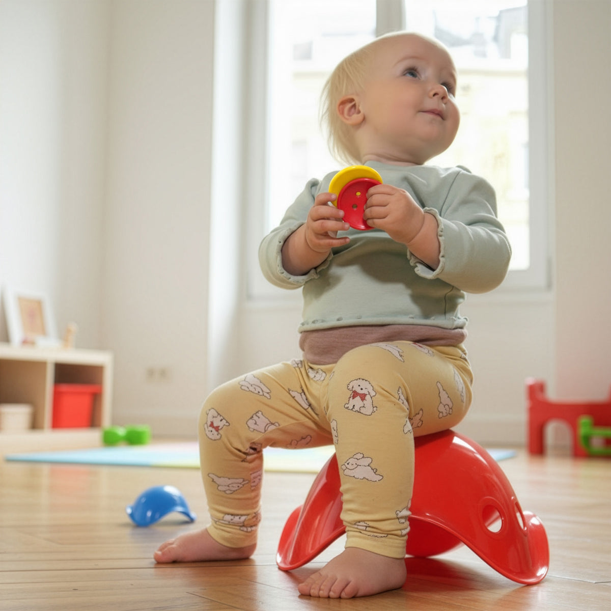 Toddler sitting on a red Bilibo chair holding a toy.