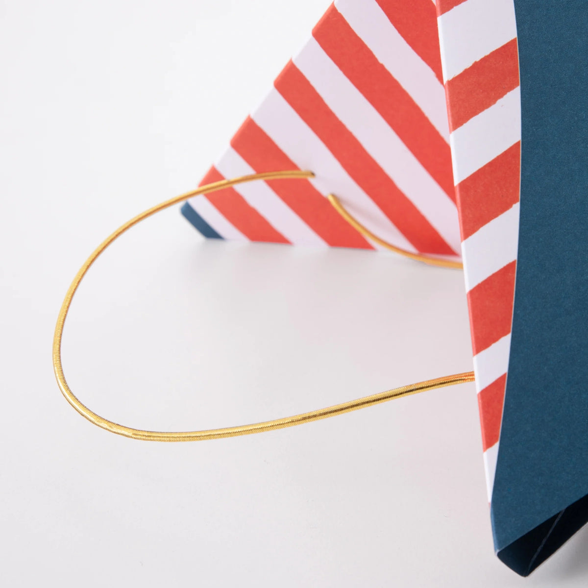 Close-up of a red and white striped gift bag with a thin gold string handle against a white background.