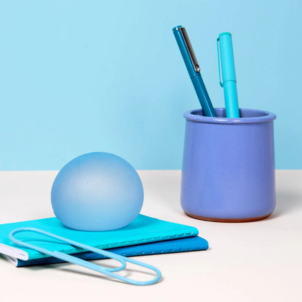 Translucent blue stress ball on notebooks next to a purple pen cup with pens.