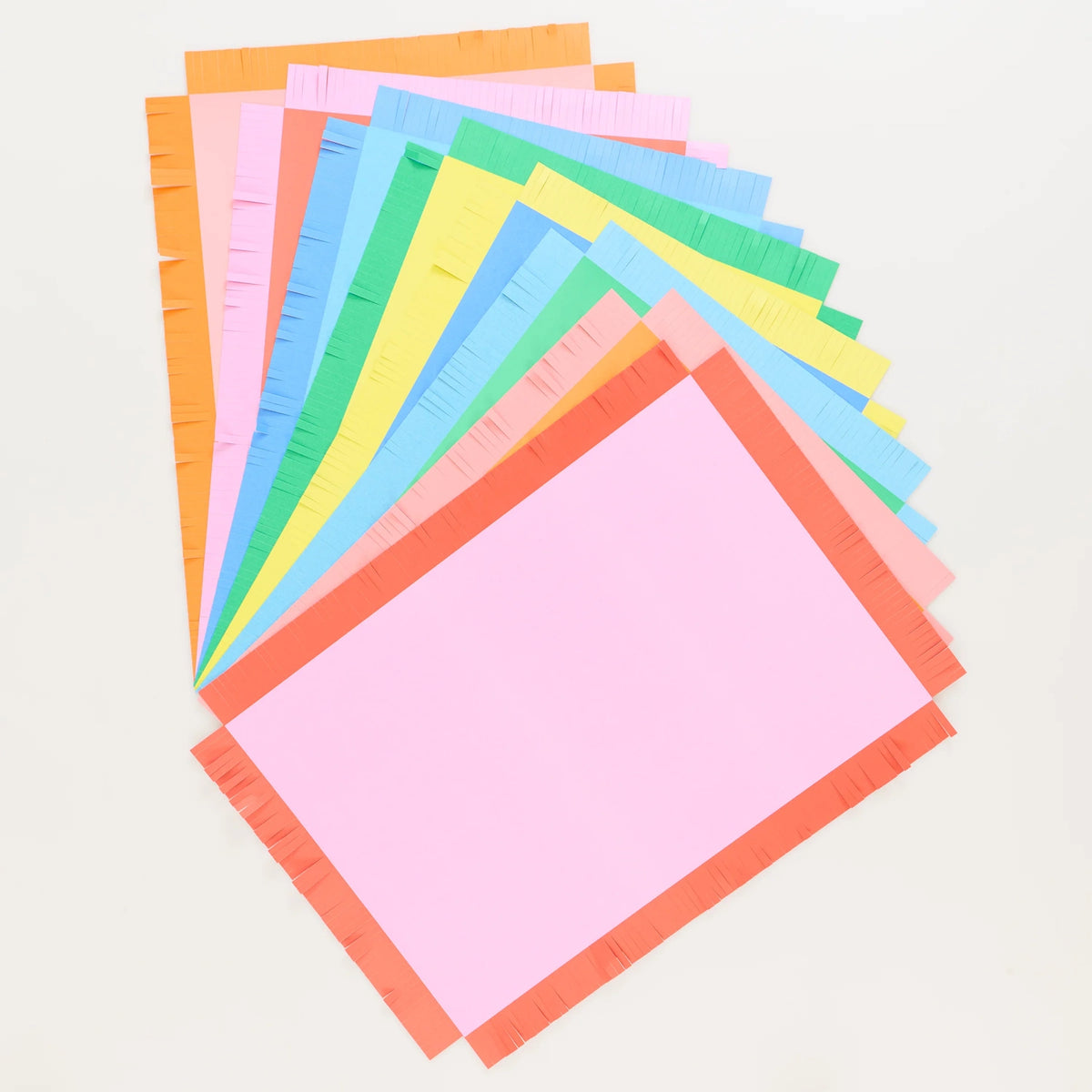 Stack of colorful paper placemats with fringed borders fanned out against a white background.
