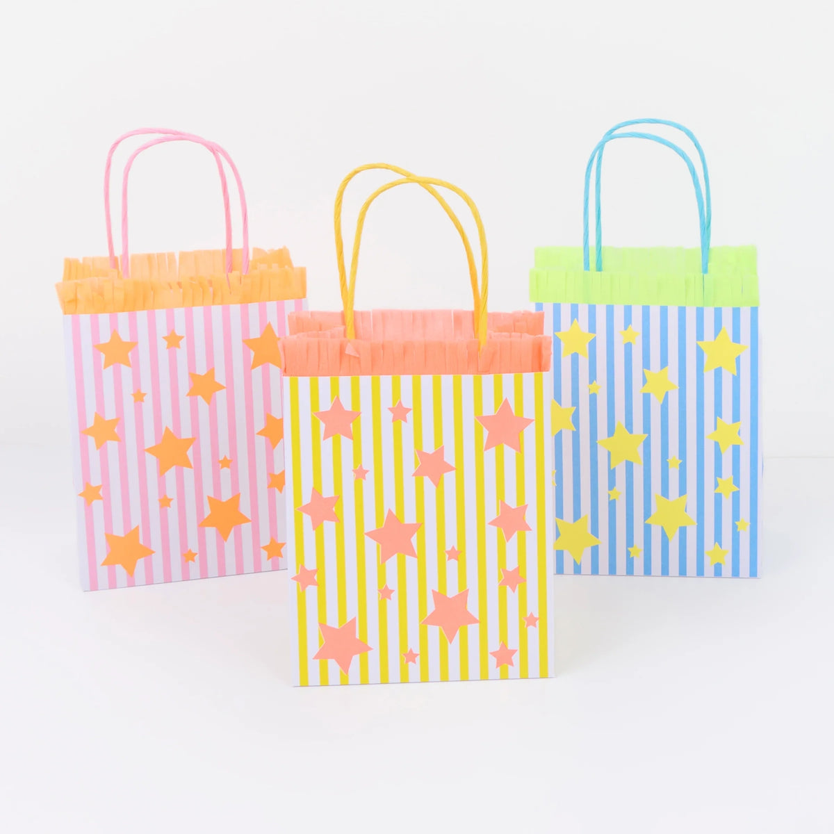 Three colorful, striped gift bags with star patterns and fringe trim against a white background.