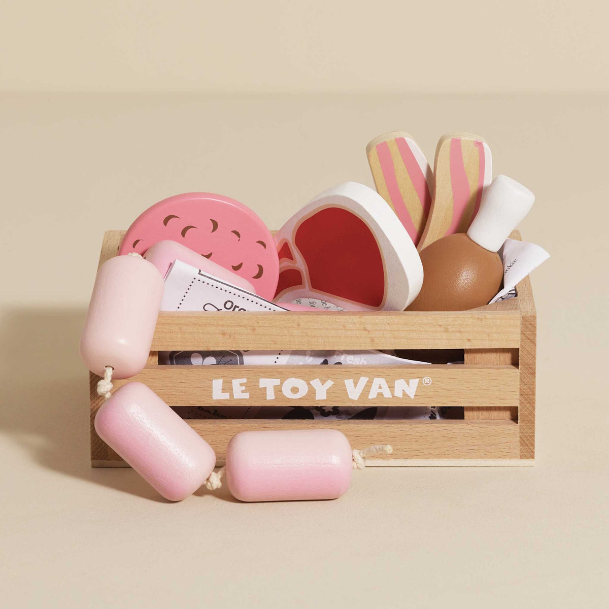 Wooden crate filled with toy meats and sausages on a beige background.