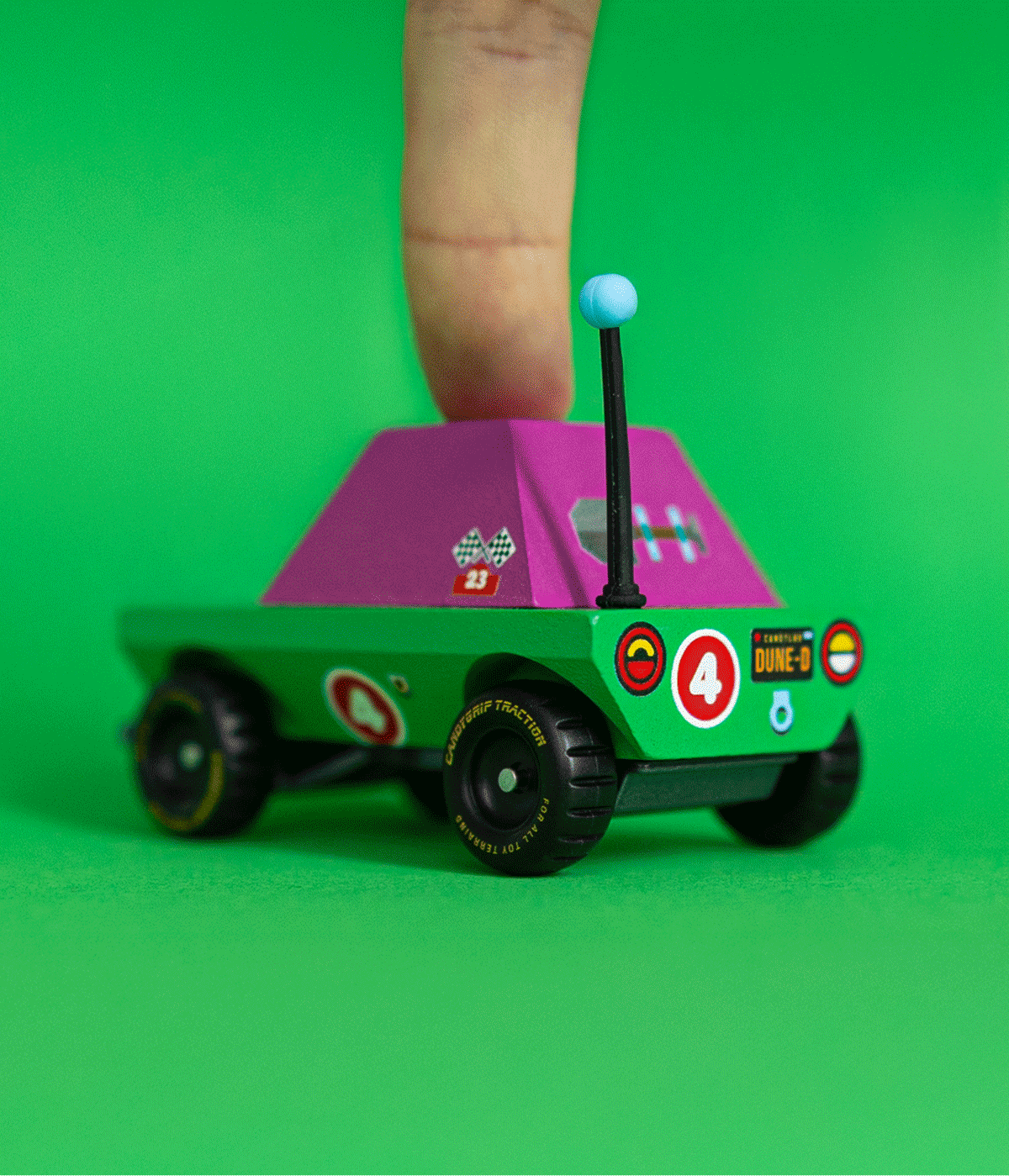 Small green and magenta toy adventure truck being pressed by a finger on a bright green background.