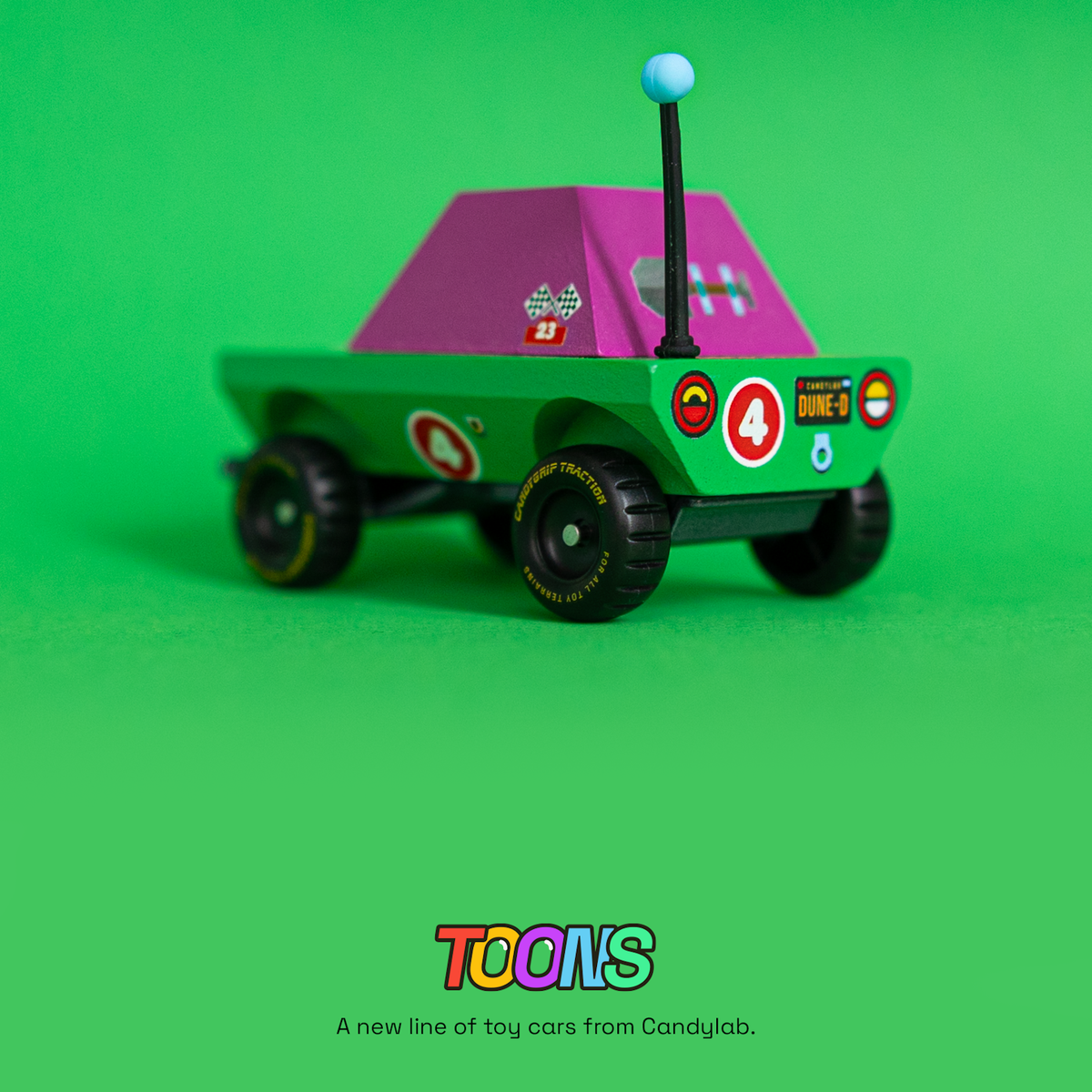 Rear view of Candylab Toons Dune-D adventure truck, a green and purple wooden toy car with a blue antenna and racing decals.