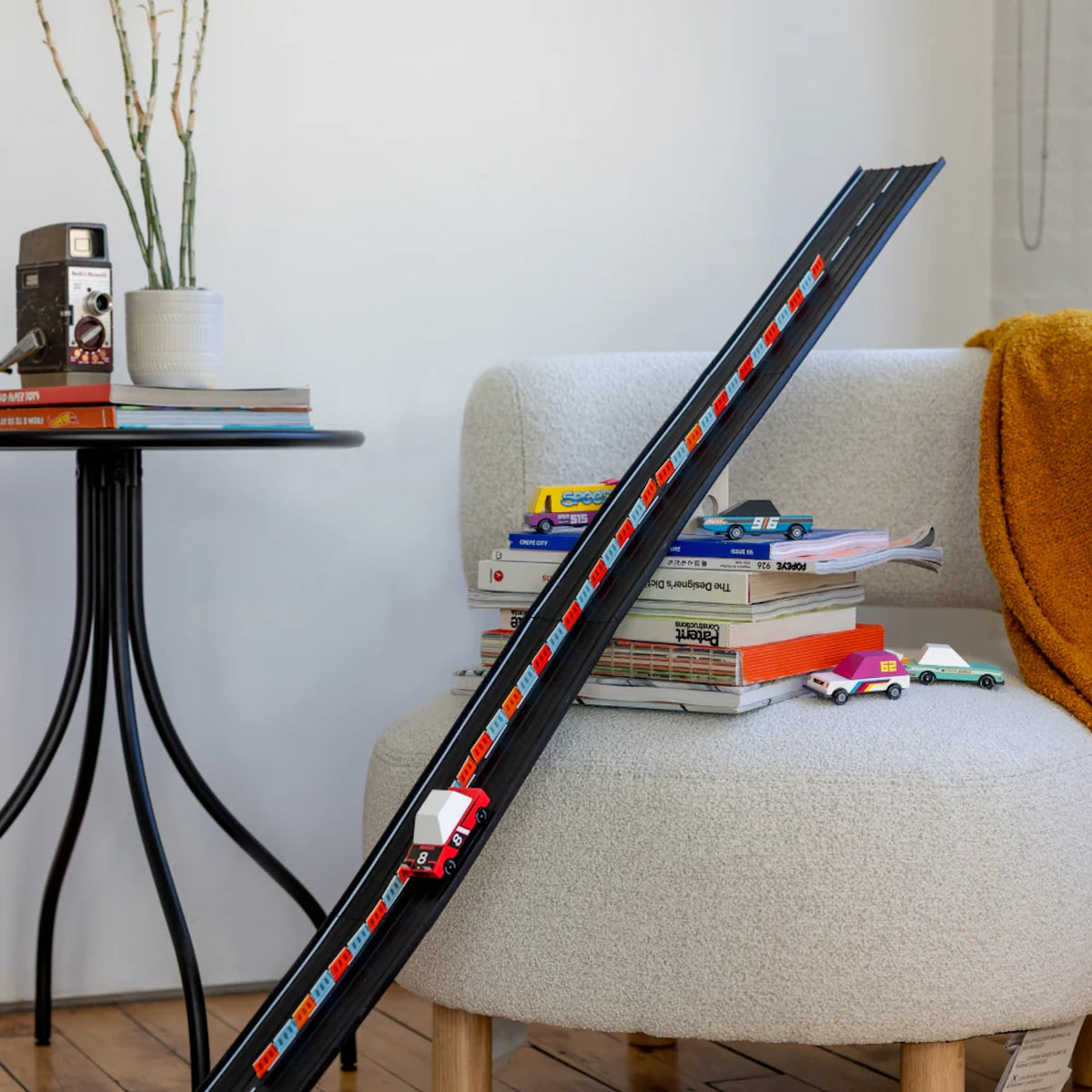 Candylab wooden toy cars racing down a long black Super Speed track leaning against a modern chair in a living room.