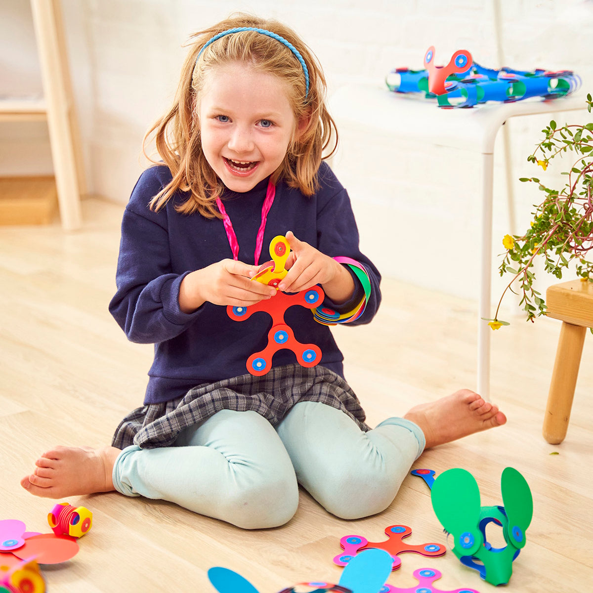 A smiling young girl sits on the floor playing with colorful magnetic building pieces.