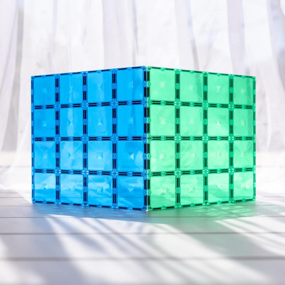 Translucent blue and green magnetic tile base plates standing upright on a sunlit surface.
