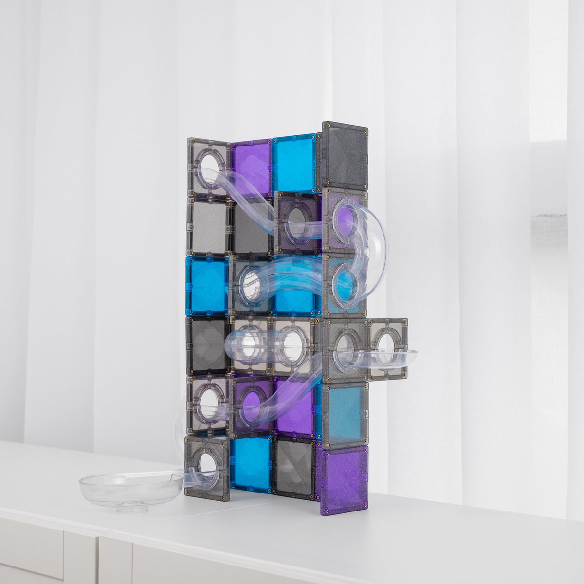 Tall ball run built with blue, purple, and glittery grey magnetic tiles and clear tubes on a white surface.