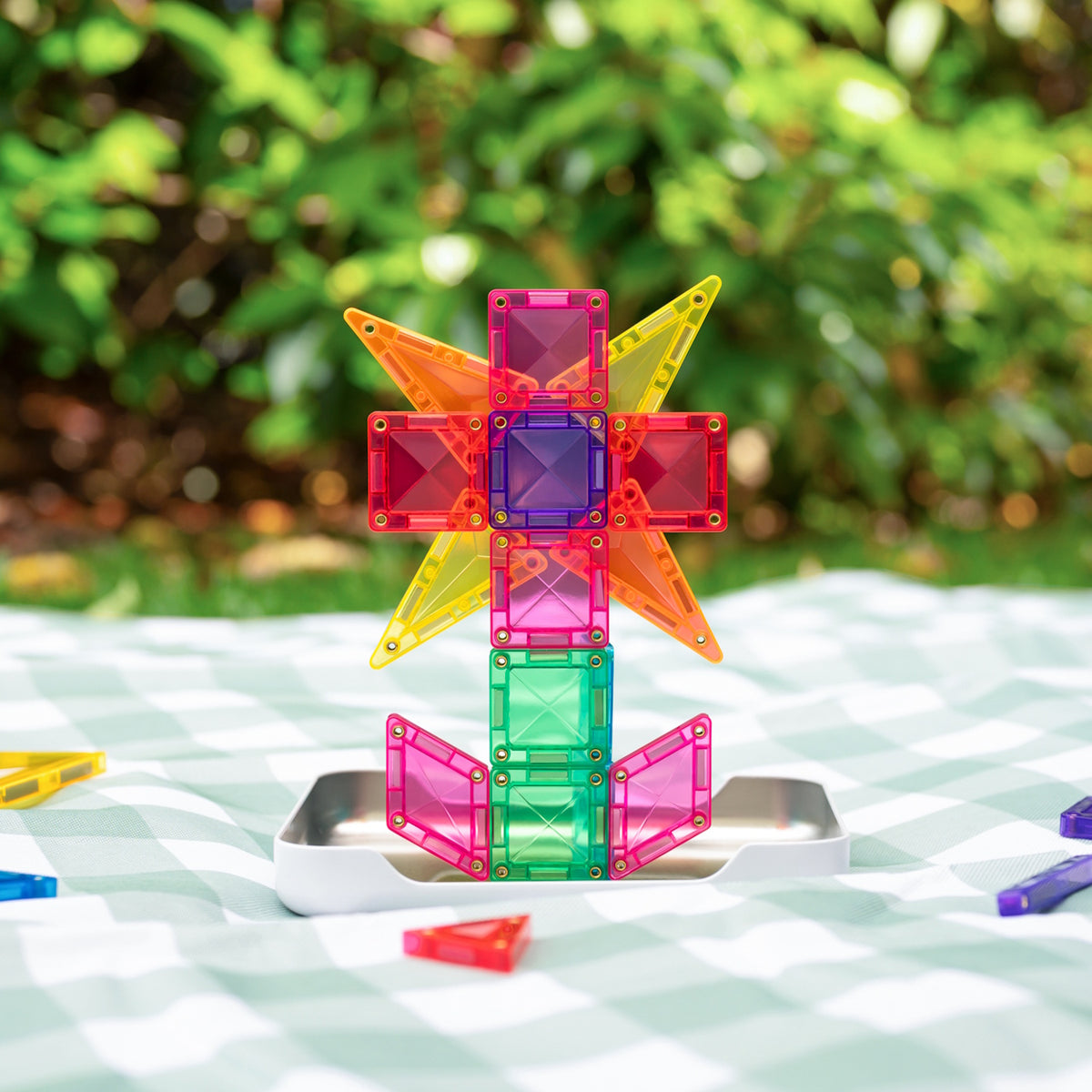 Colorful magnetic tiles built into a flower structure resting on a green checkered picnic blanket.