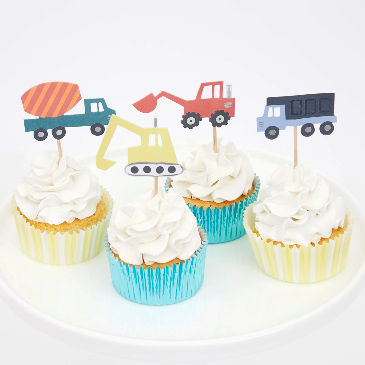 Cupcakes with swirled white frosting, construction vehicle toppers, and shiny striped baking cups on a white plate.