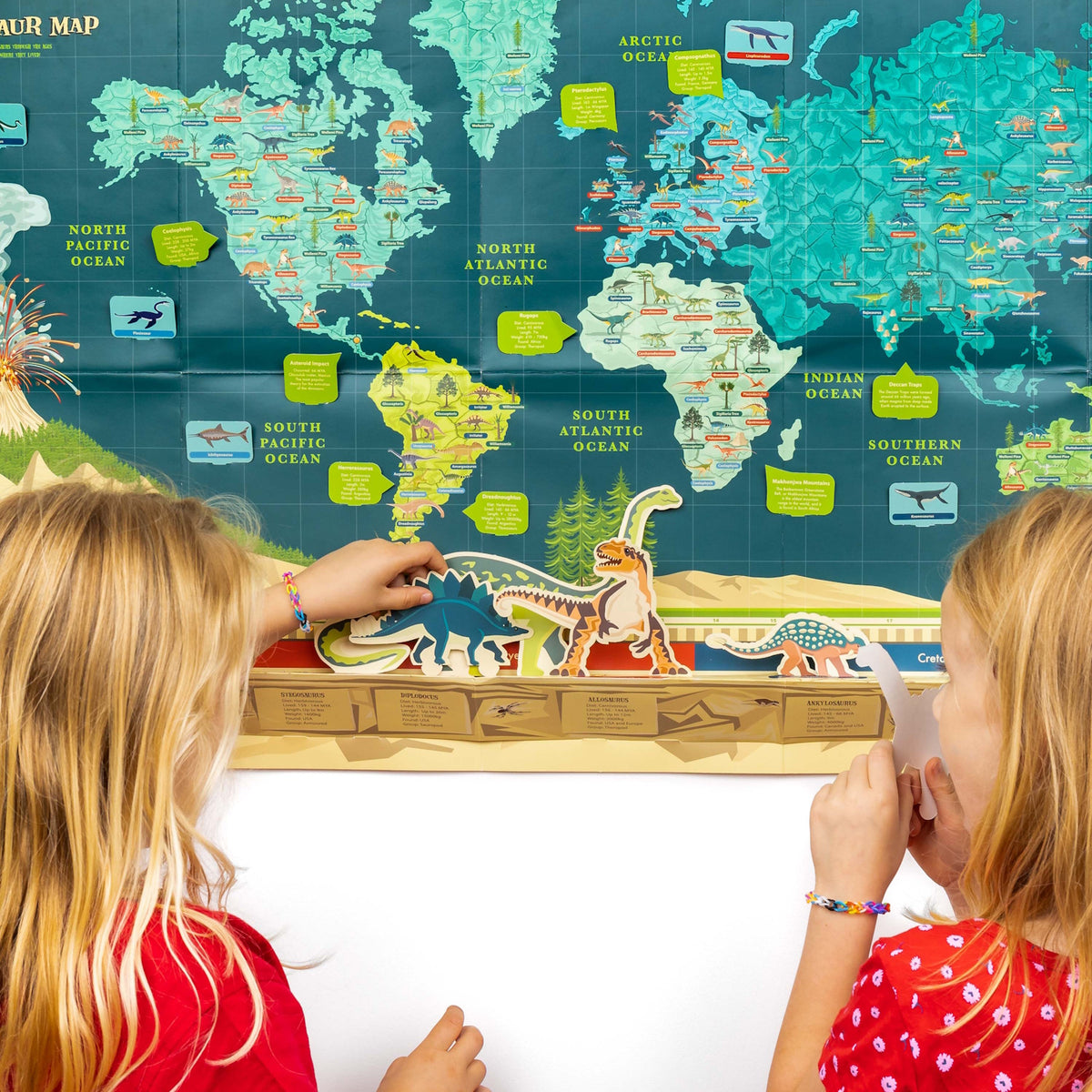 Two young girls interacting with a dinosaur timeline activity set in front of a illustrated world map.