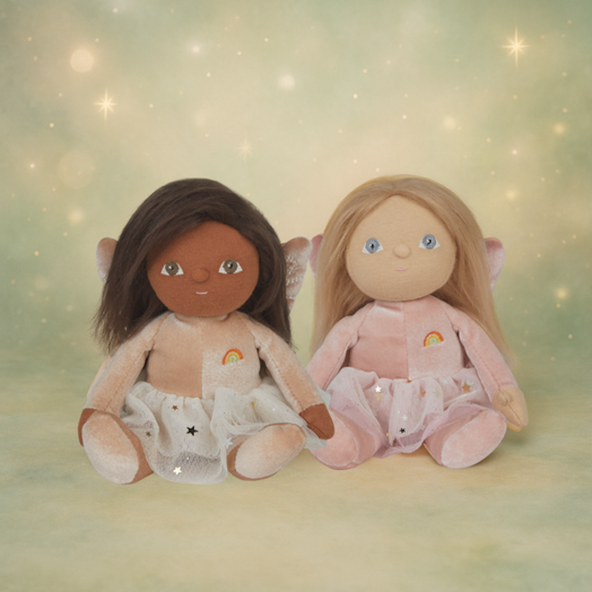 Two Olli Ella Dinky Dinkum fairy dolls with wings sitting together against a sparkling green background.