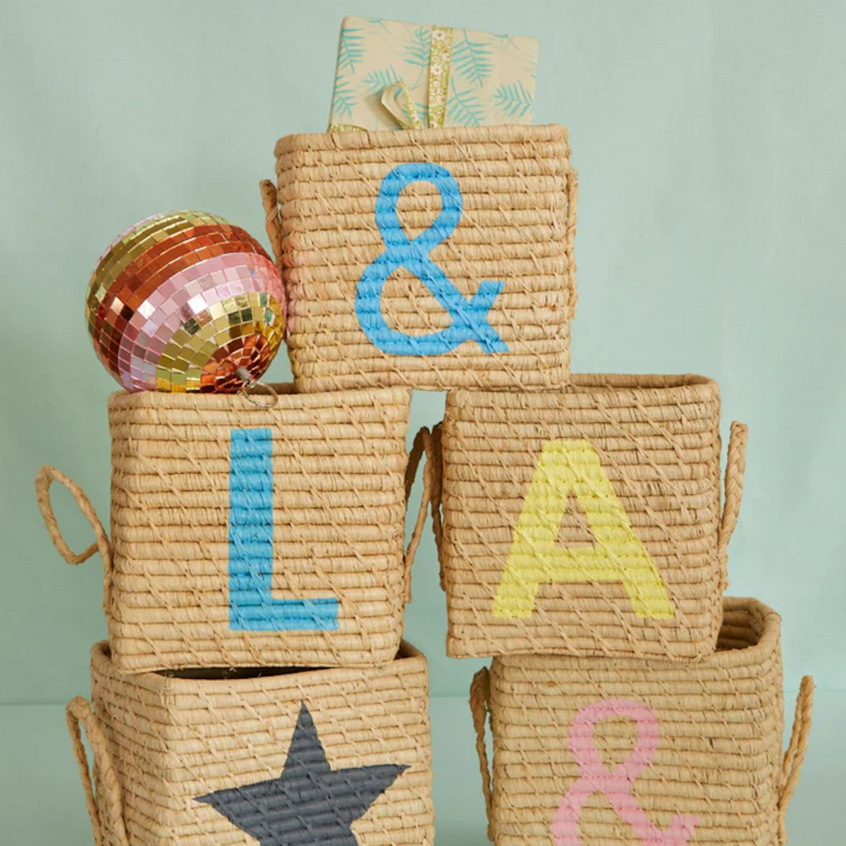 Stacked woven baskets painted with letters, symbols, and a star, topped with a colorful disco ball.