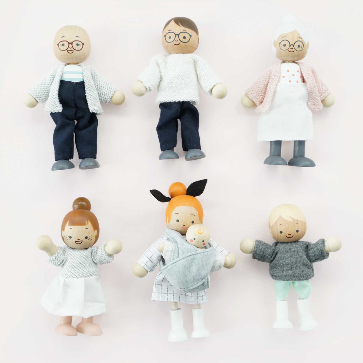 Seven wooden dollhouse family figures arranged in two neat rows against a light pink background.