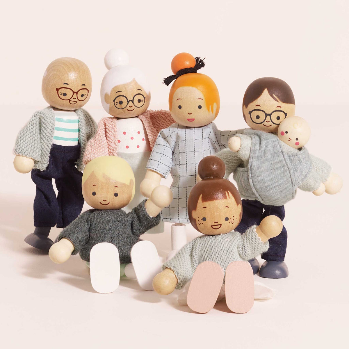 Close-up of seven wooden dollhouse family figures sitting and standing against a pale pink background.