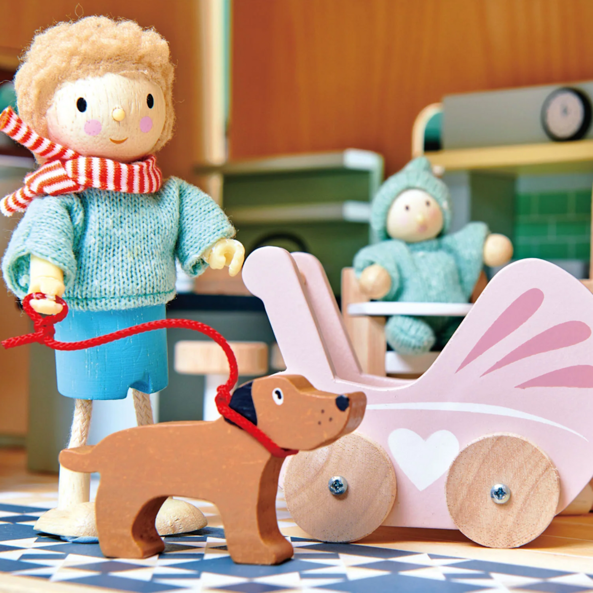 A wooden figure holds a red leash with a toy dog next to a pink pram and baby doll.
