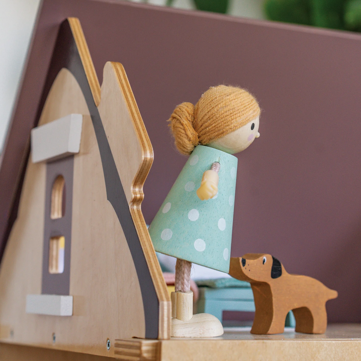 A wooden doll in a polka-dot dress stands beside a small toy dog on a dollhouse balcony.