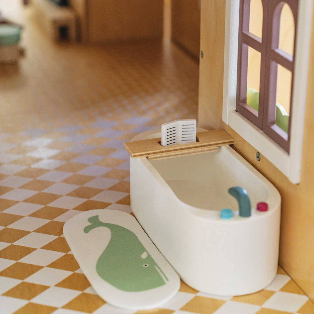 Dollhouse white bathtub with a tiny book on a wooden tray, next to a green whale bath mat.