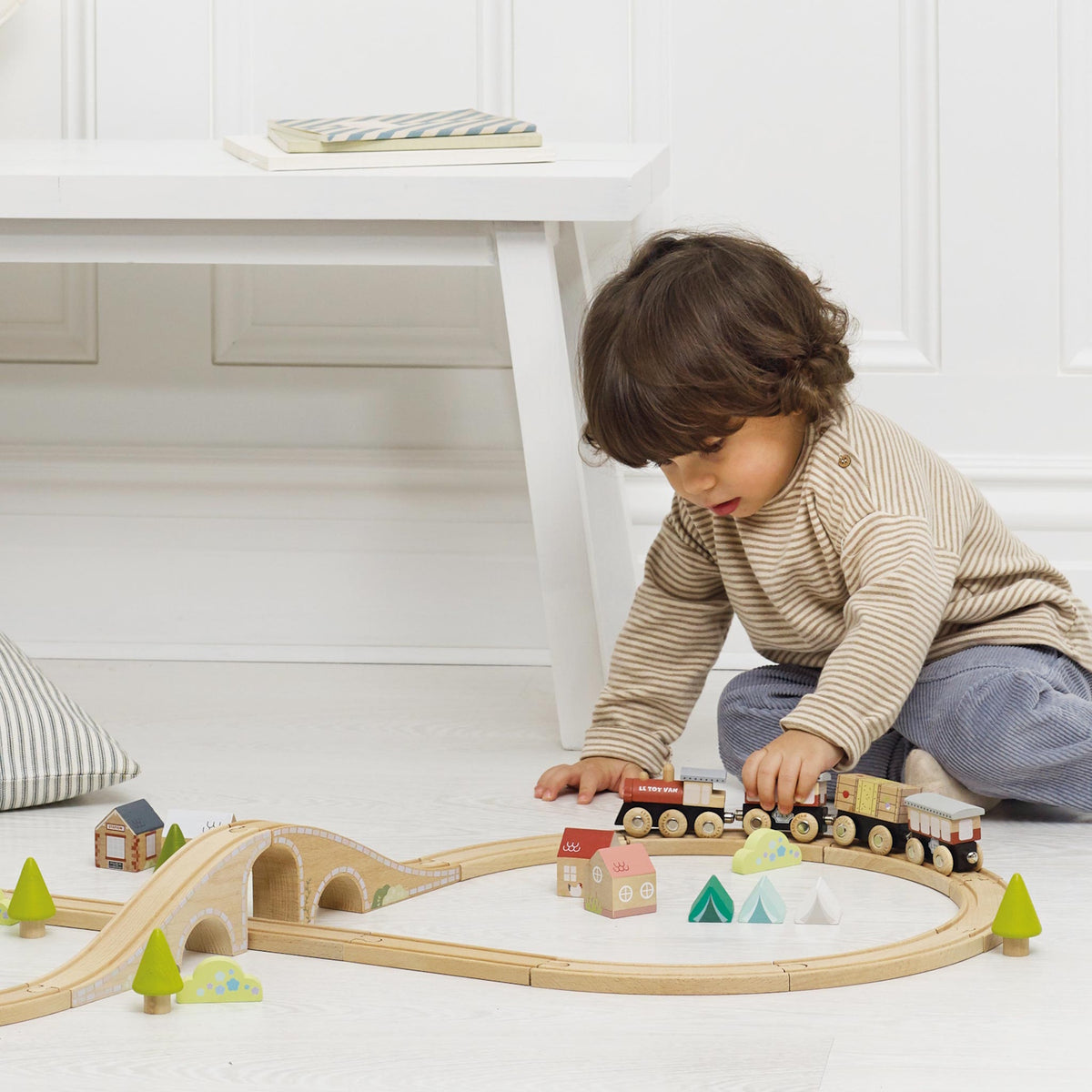 Young child playing with a wooden toy train set on the floor.