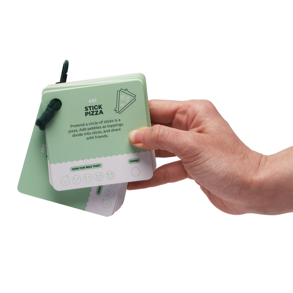 Hand holding a green activity card booklet showing the "Stick Pizza" card prompt.