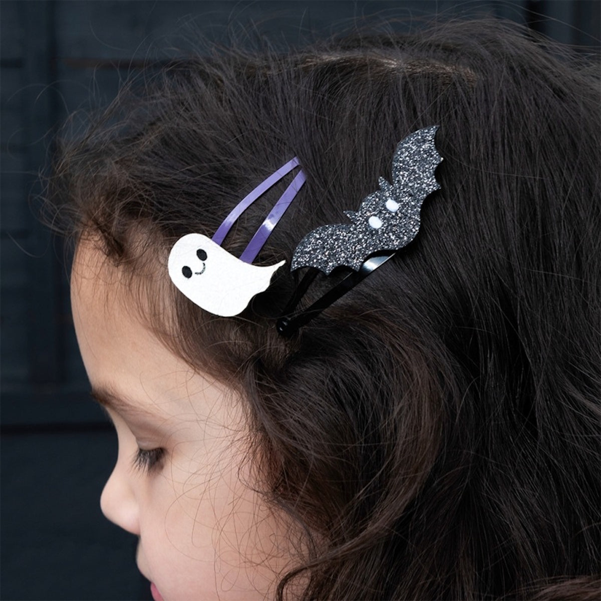 Close-up of a child wearing a glitter ghost and a black bat hair clip side by side.