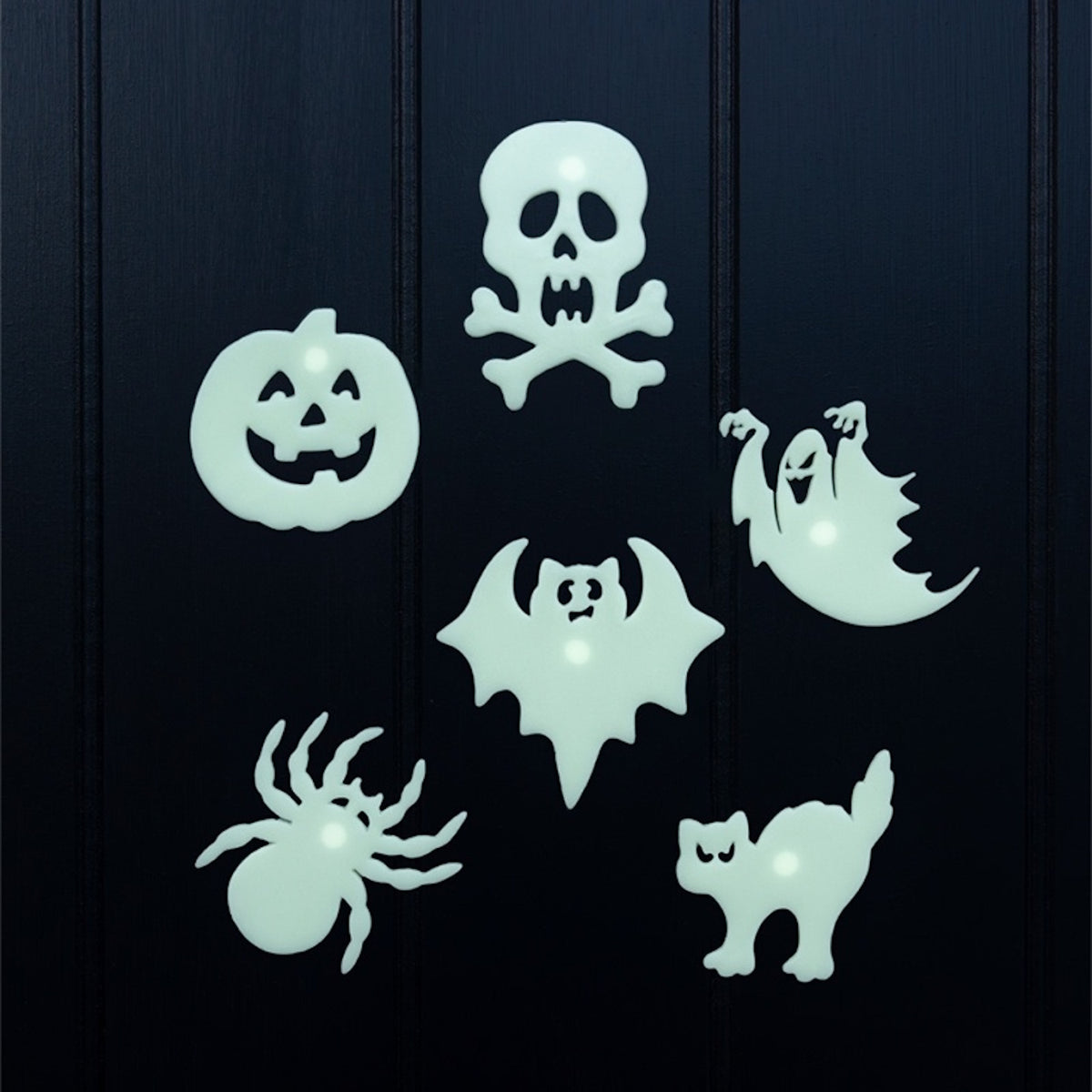 Six glow-in-the-dark Halloween stick-on shapes displayed on a dark wooden surface.