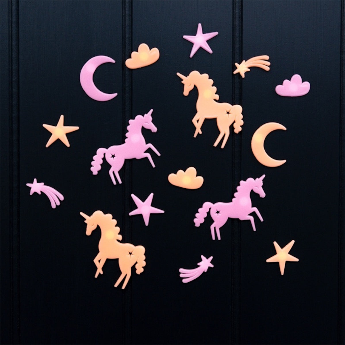Pink and yellow glow-in-the-dark unicorn, star, and crescent moon shapes on a dark wall.