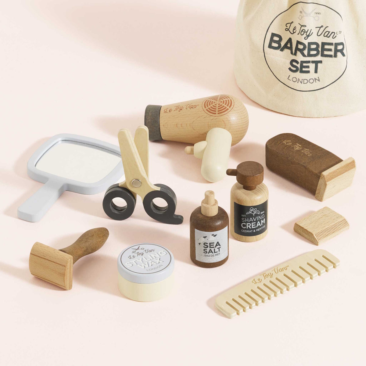 Wooden toy barber kit with hair dryer, scissors, bottles, combs, mirror, and drawstring bag.
