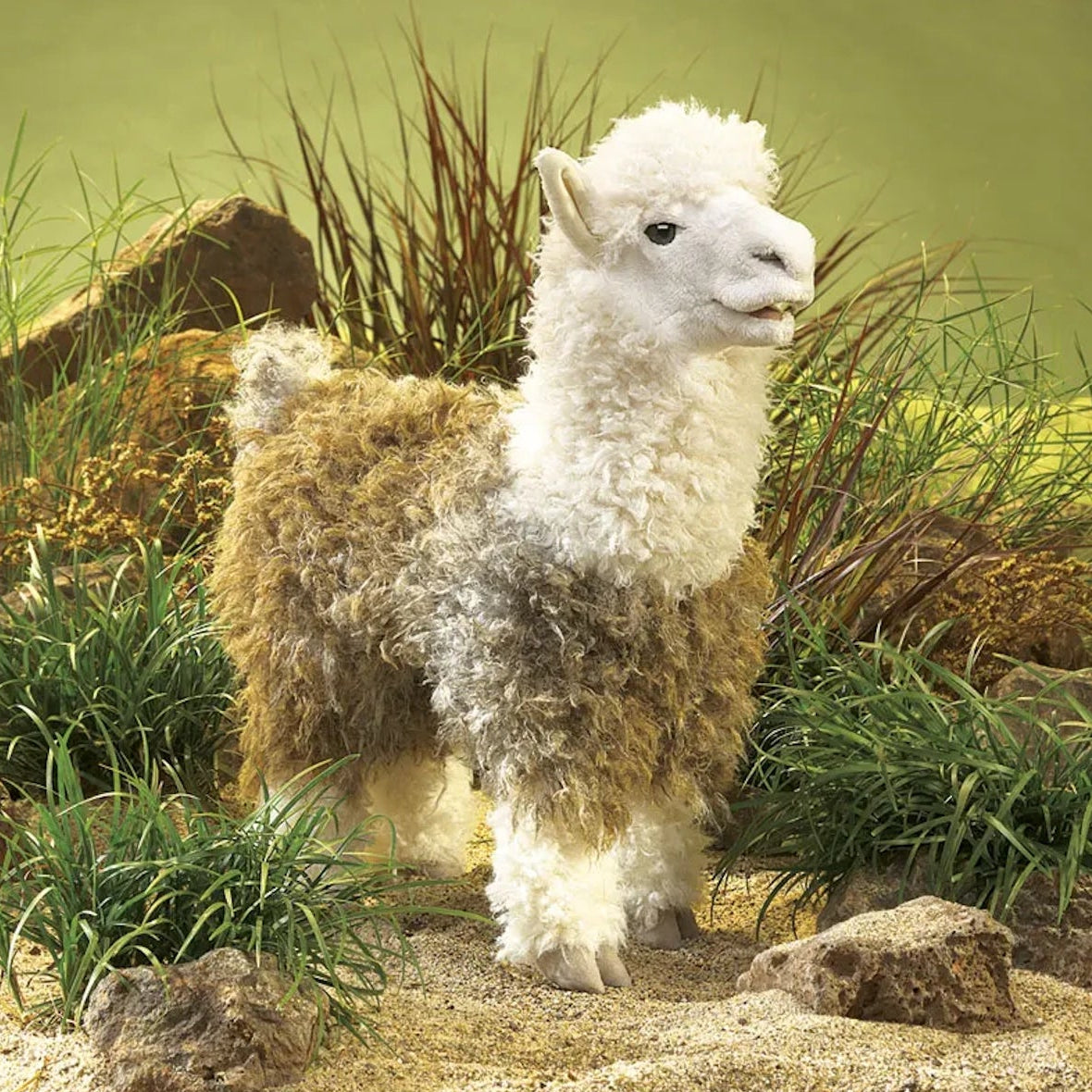 Alpaca hand puppet standing outdoors among rocks and grassy foliage.