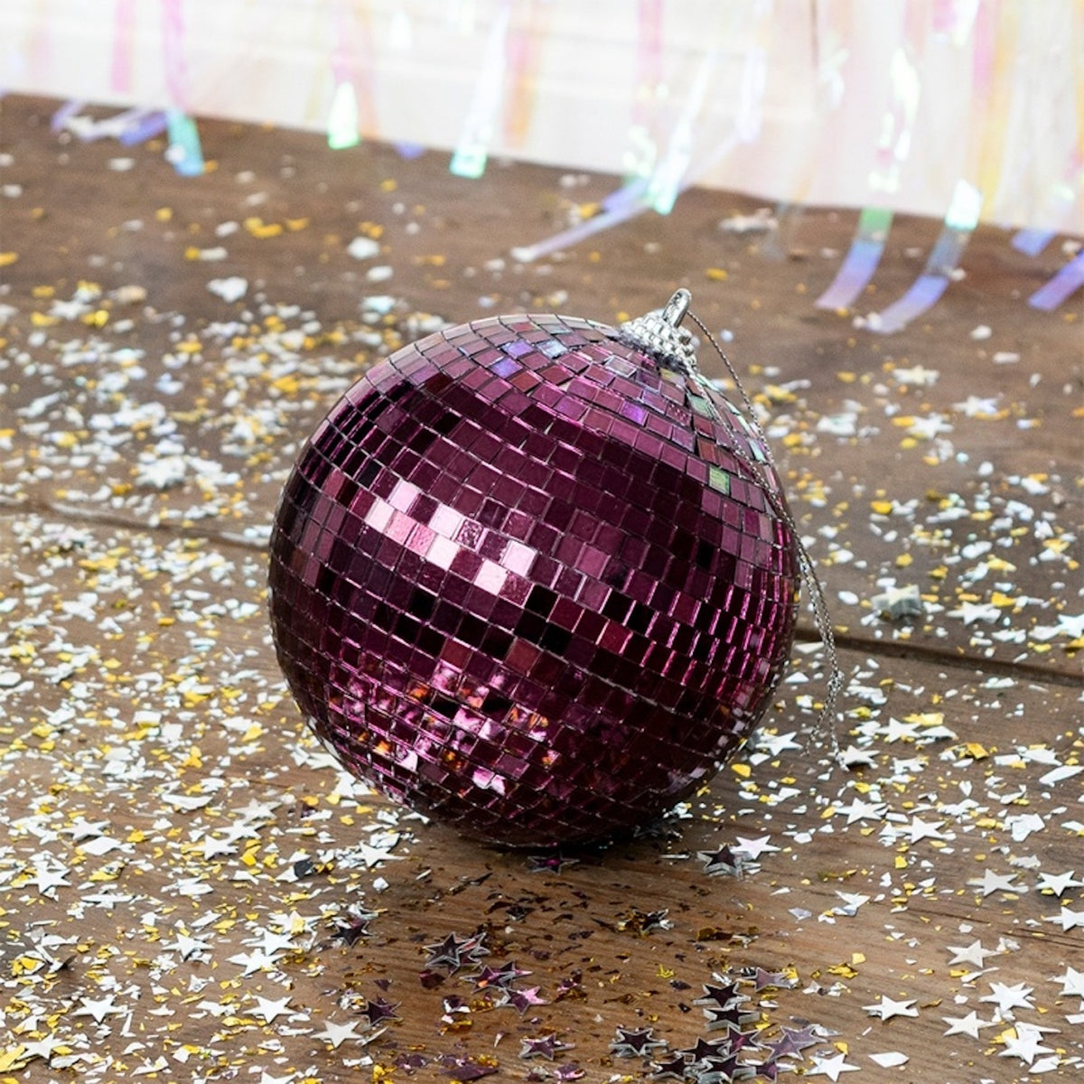 A plum purple disco ball rests on a wooden floor scattered with silver and gold star confetti.