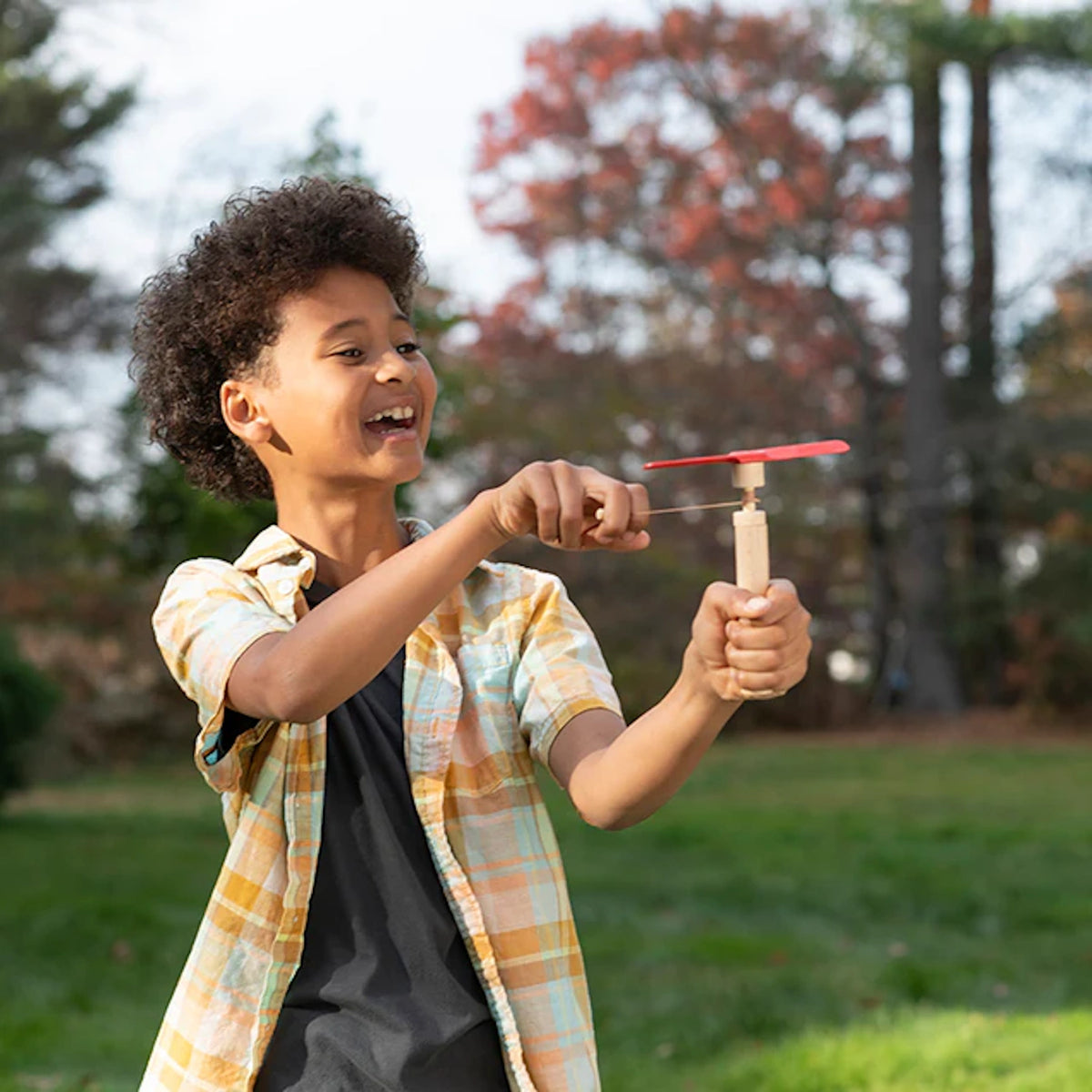 Young boy outdoors playing with a Huckleberry wooden pull-string helicopter toy featuring red propeller blades.