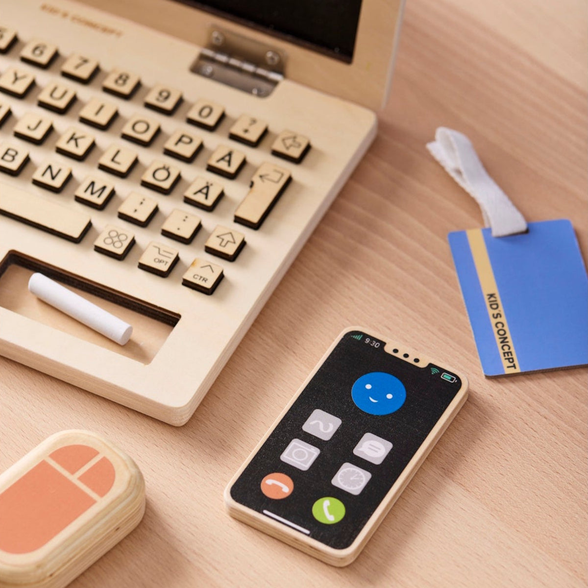 Wooden toy laptop play set with a toy smartphone, mouse, and ID badge on a desk.