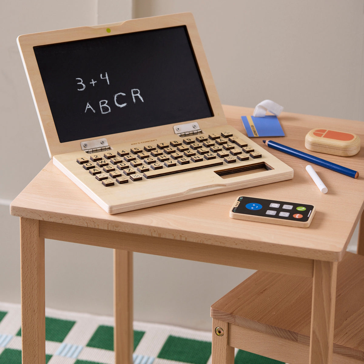 Open wooden toy laptop with chalkboard screen and accessories on a child's desk.