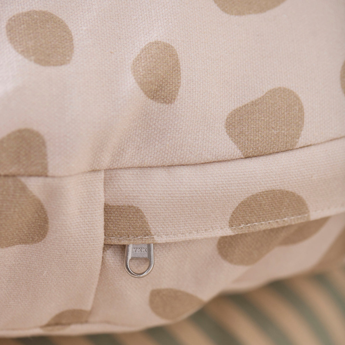 Close-up of a beige cushion with brown spots and a silver YKK zipper.