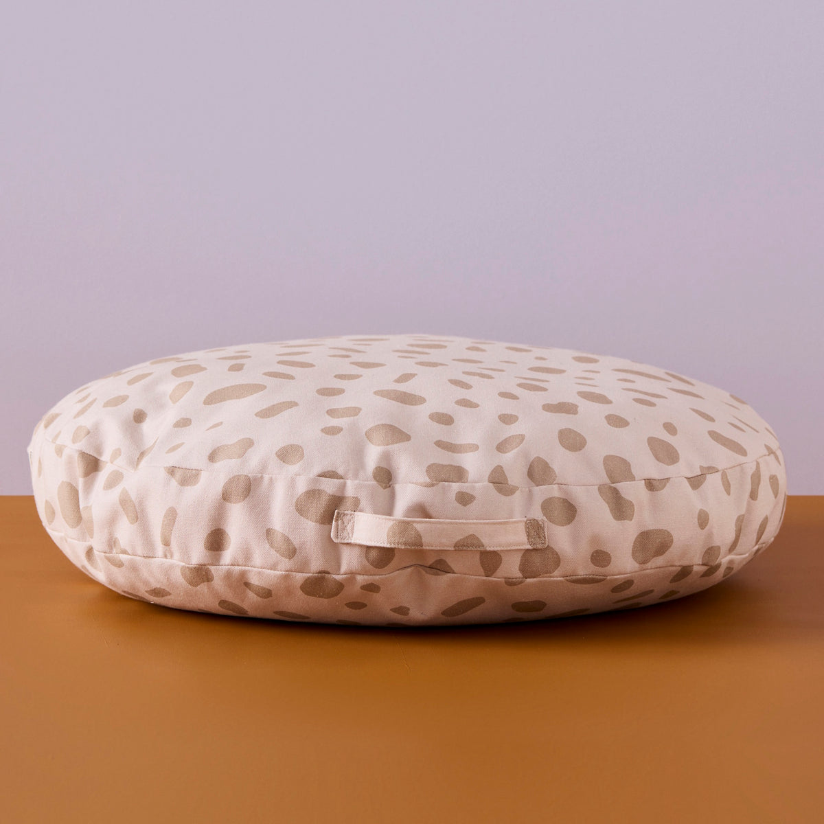 Round cream floor cushion with a beige spotted pattern and a side handle.