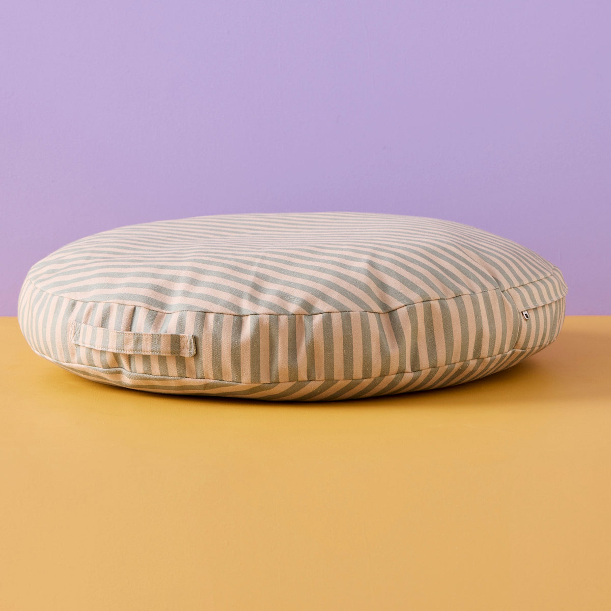 Round sage green and beige striped floor cushion with a fabric handle against a two-tone background.