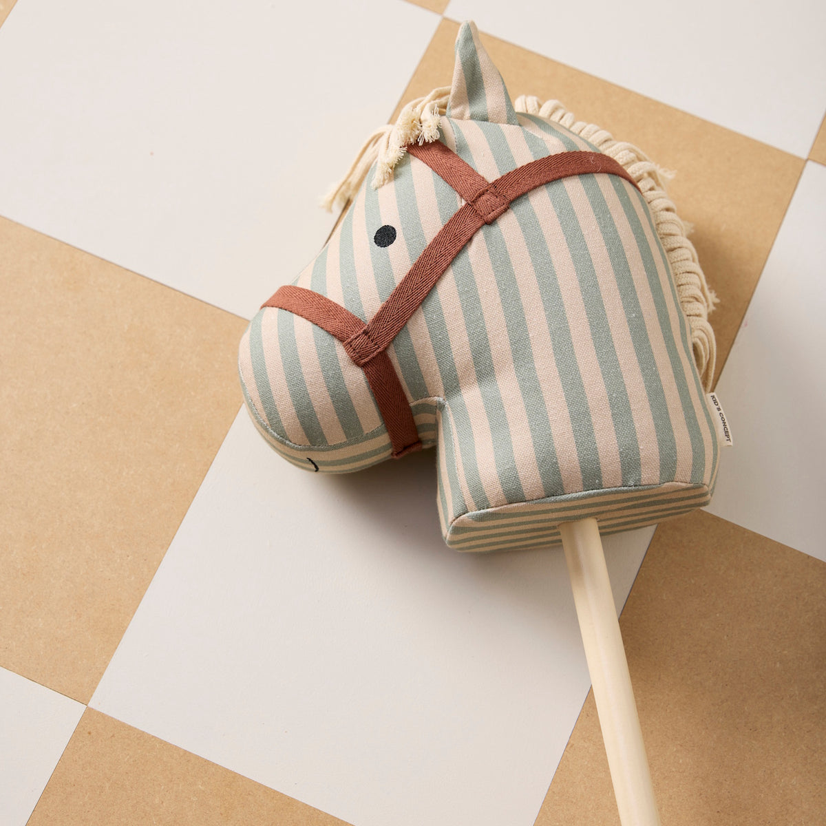 Striped fabric hobby horse head on a wooden stick lying on a tiled floor.