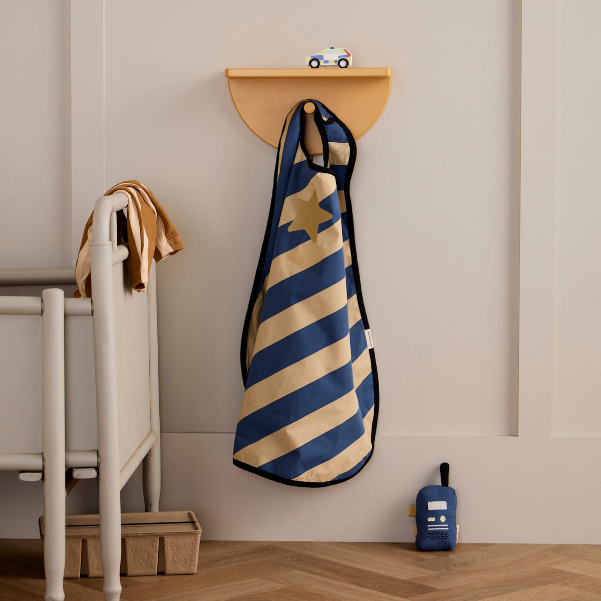 Blue and yellow striped dress-up cape hanging on a wall hook with a toy walkie-talkie below.
