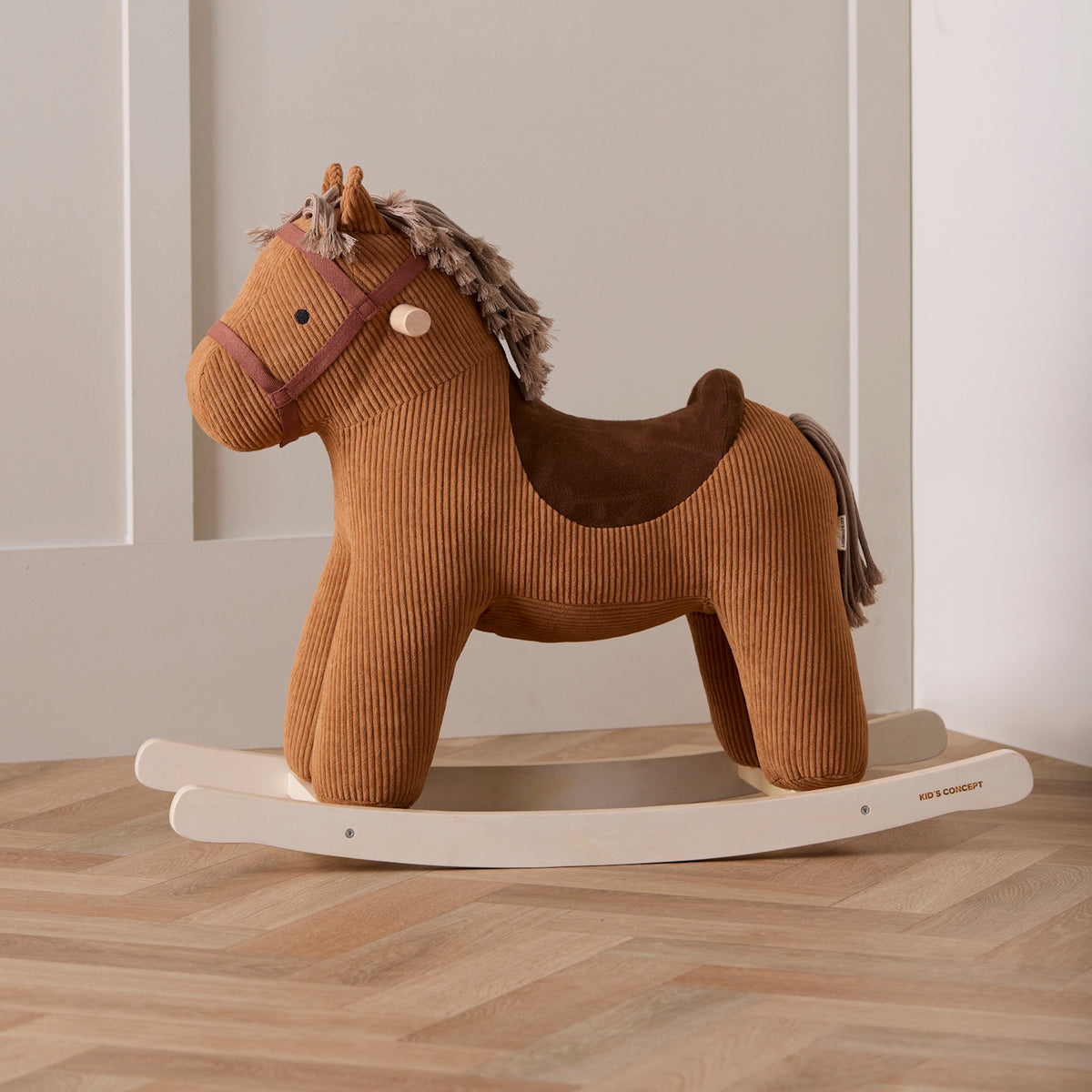 Brown corduroy plush rocking horse on a light wood rocker base, set against a neutral wall.