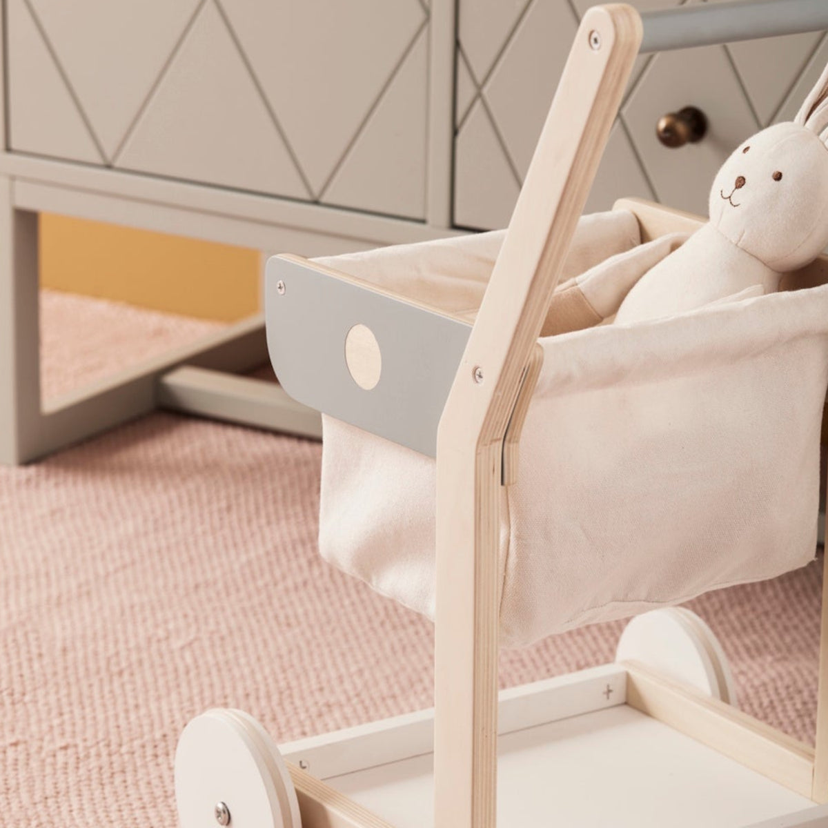 Wooden toy shopping trolley with a stuffed bunny sitting inside the fabric basket.