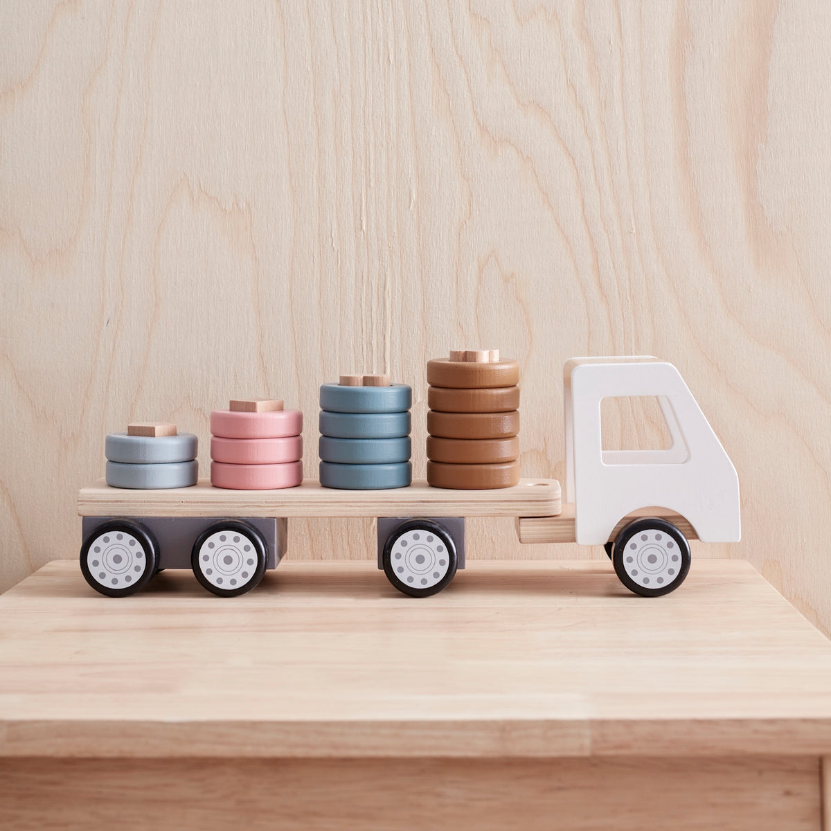 Side view of a wooden toy truck with colorful shape-sorting rings stacked on its flatbed trailer.