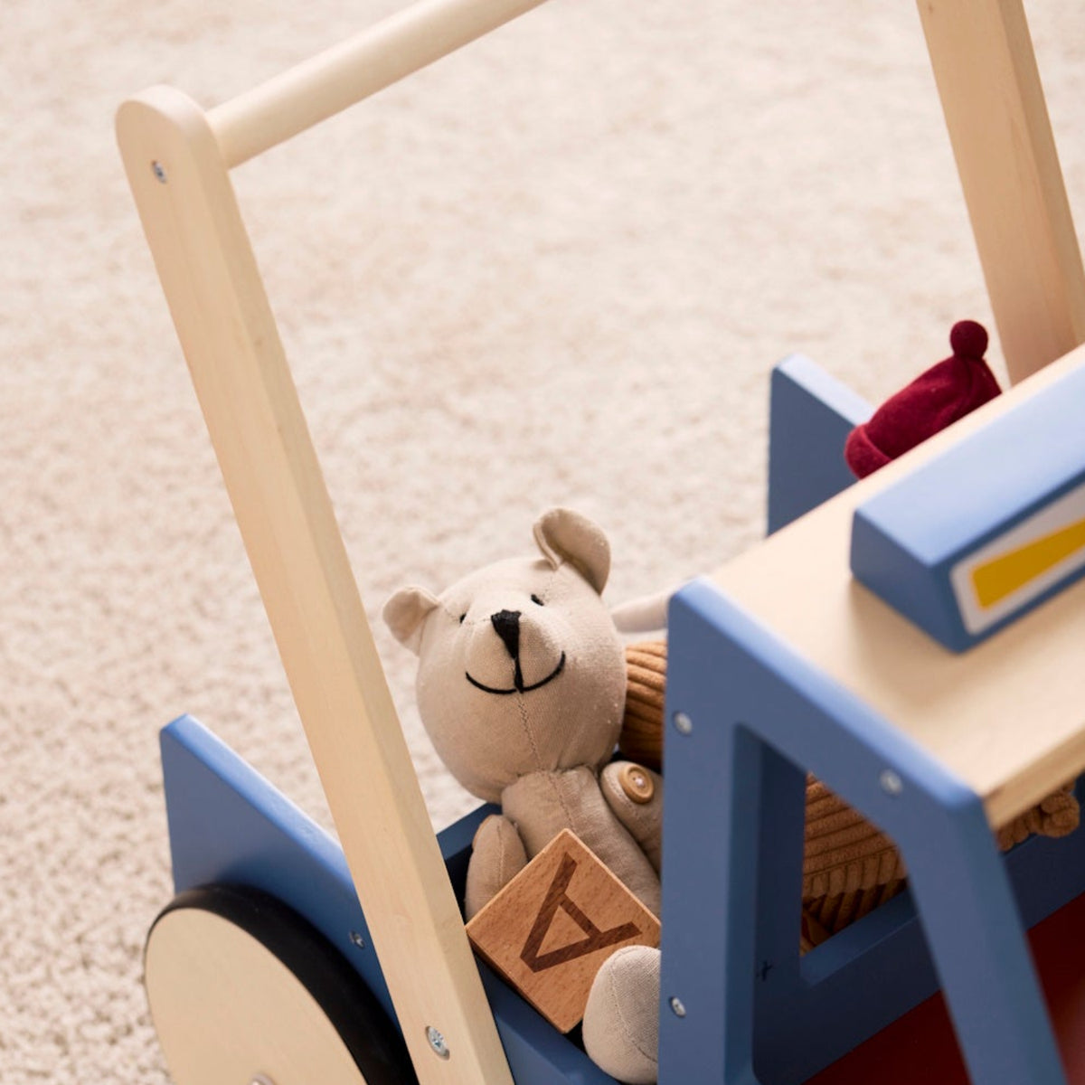 Close-up view of a blue wooden toy walker truck with a stuffed teddy bear and wooden blocks inside.