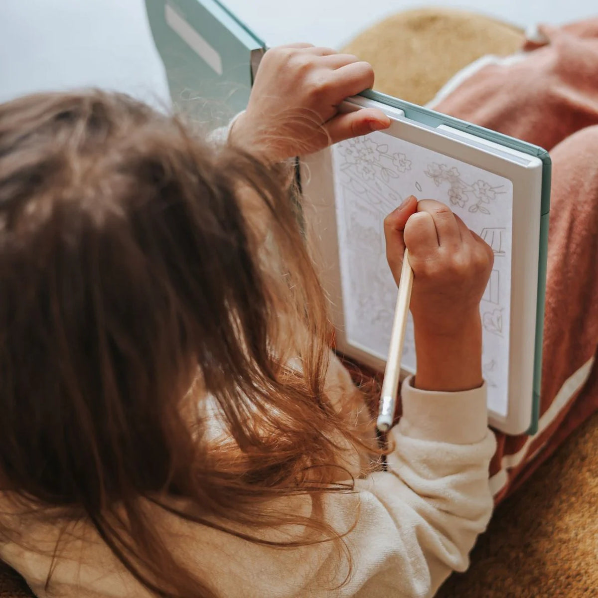An over-the-shoulder view of a child using a pencil to trace a drawing on an illuminated light pad.
