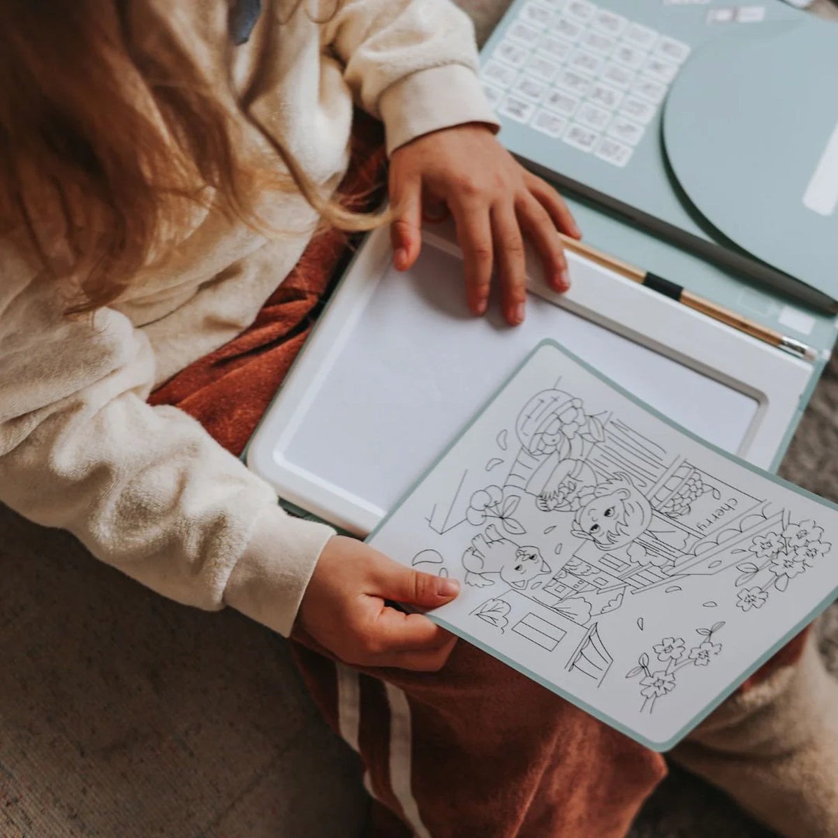 A child holding a drawing sheet over a light-up drawing pad in their lap.