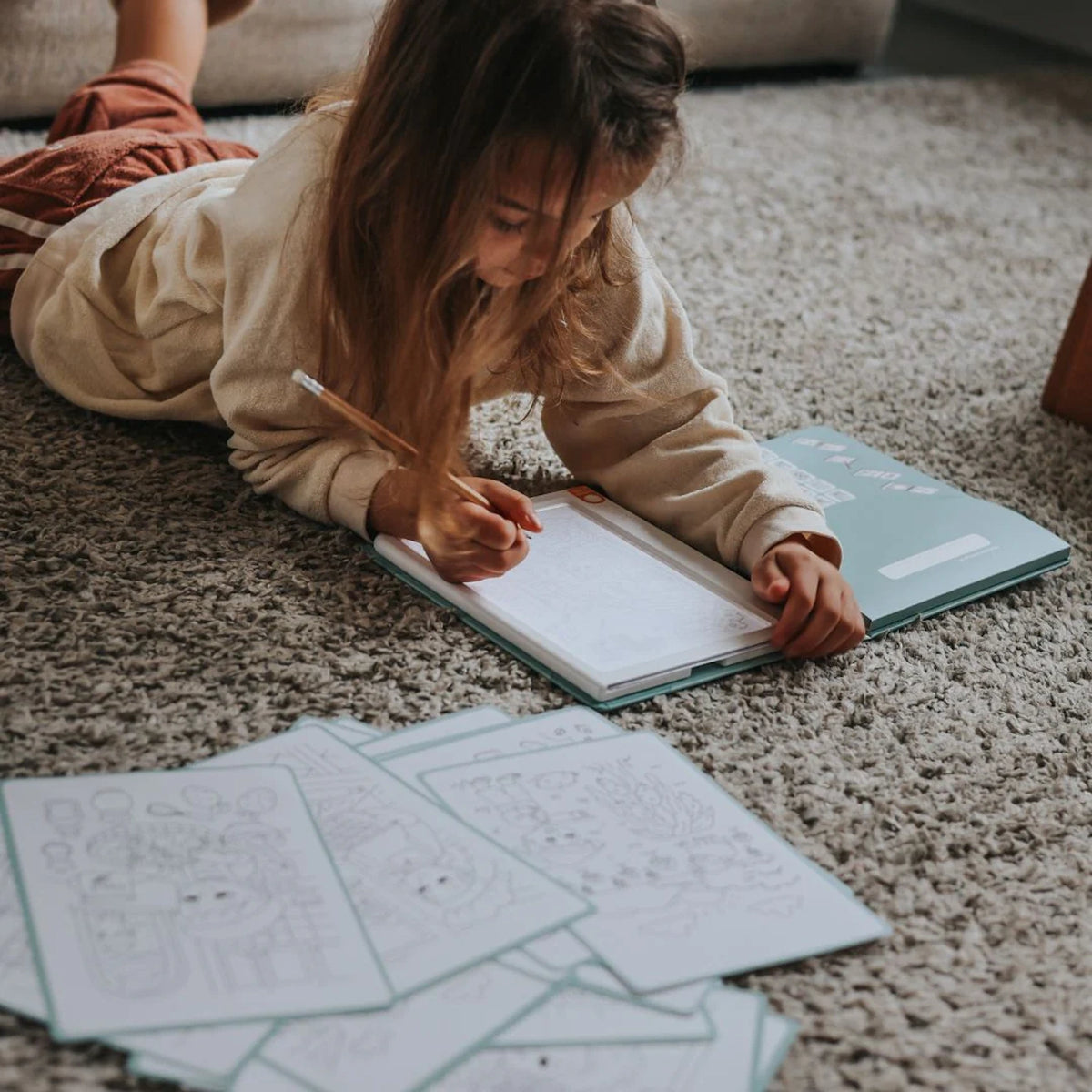 Young girl lying on a rug drawing on a Kidywolf illuminated pad with tracing papers scattered nearby.